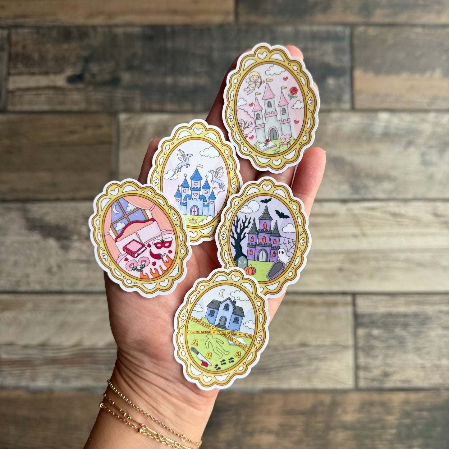 Hand holding five decorative stickers with intricate designs against a wooden background